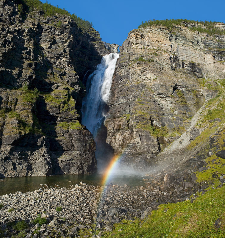 In the sunlight a rainbow shines at the base of the waterfall  © Bård Løken