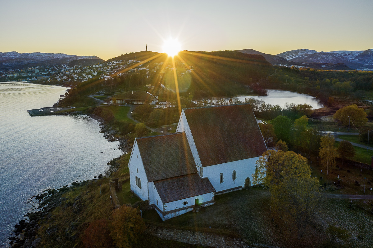 Trondenes kirke i lav høstsol, Trondenes historiske senter og vatnet Laugen © Jan Schmitt