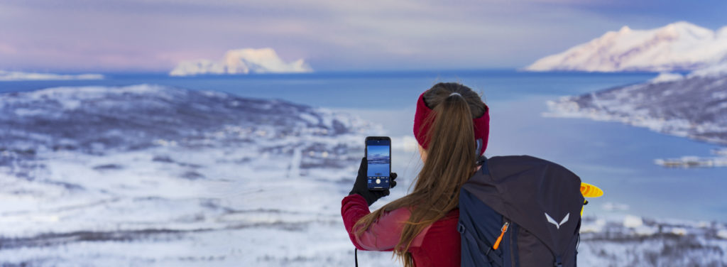 Girl taking pictures of a snow covered fjord