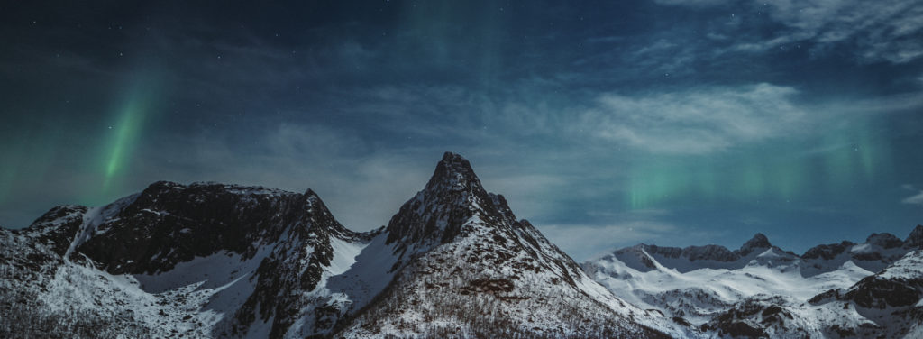 Soft northern lights over a the top of a mountain chain.