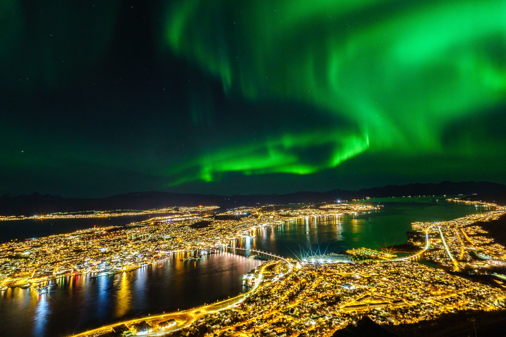 A view from the city mountain Fløya over Tromsø towards the northern lights dancing in the northwest © Vegard Stien / Raw Studios
